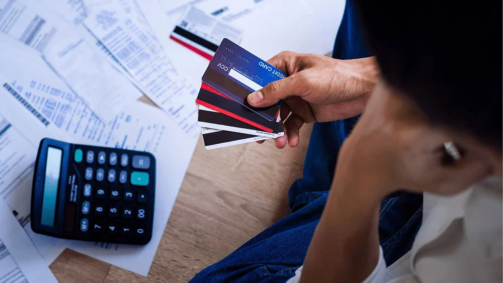 ersona estresada revisando tarjetas de crédito y facturas para salir de deudas.